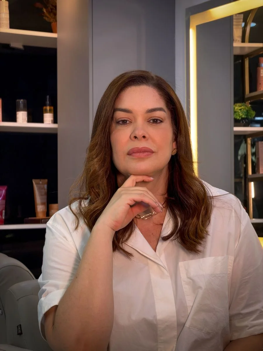 Shirley Diniz, dona e cabeleireira do Studio, de camisa branca com a mão apoiada no queixo